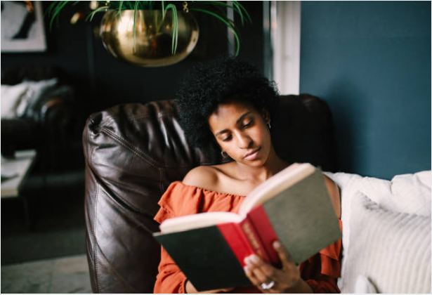 Una mujer lee un libro sentada en un sillón.